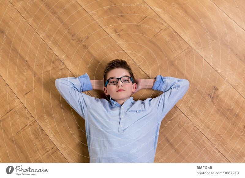 Teenager with glasses lies relaxed on wooden floor at home teenager Boy (child) Eyeglasses Lie Ground Wooden Boys Parquet floor Homeschooling Upper body Teenie