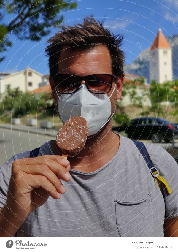 Young guy on summer vacations wearing corona virus protective face mask not beeing able to lick ice cream bar. Ice cream Summer Candy Delicious Sweet Food