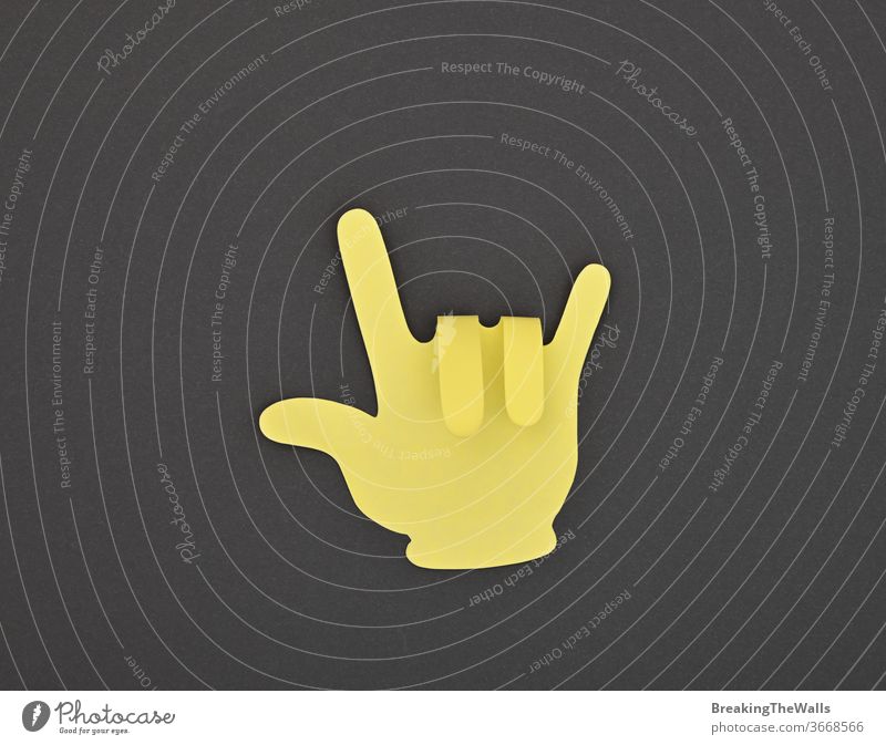 Paper made yellow HORNS gesture sticker on grey Horns devil rock music metal hard heavy good hand shape fingers paper closeup note black background dark