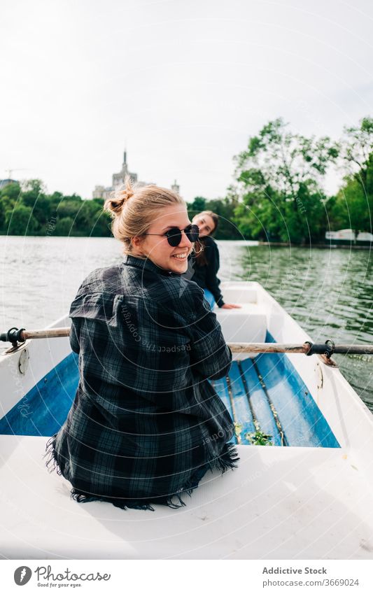 Cheerful girlfriends rowing on boat on lake surface women positive cheerful sculling oar smile nature activity peaceful calm relax summer together happy leisure