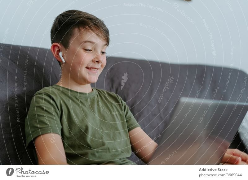 Adorable kid having video call on laptop at home boy video chat communicate wave hand sofa cheerful gadget happy internet device child little wireless earphones