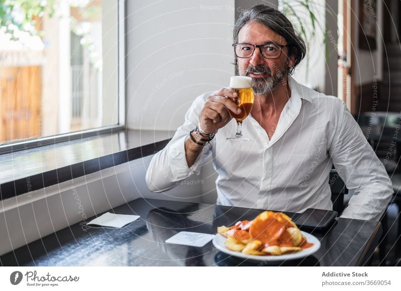 Bearded ethnic man eating delicious lunch in restaurant elderly cafe glass beer mature drink positive male smile aged retire bar chill meal eyeglasses beverage