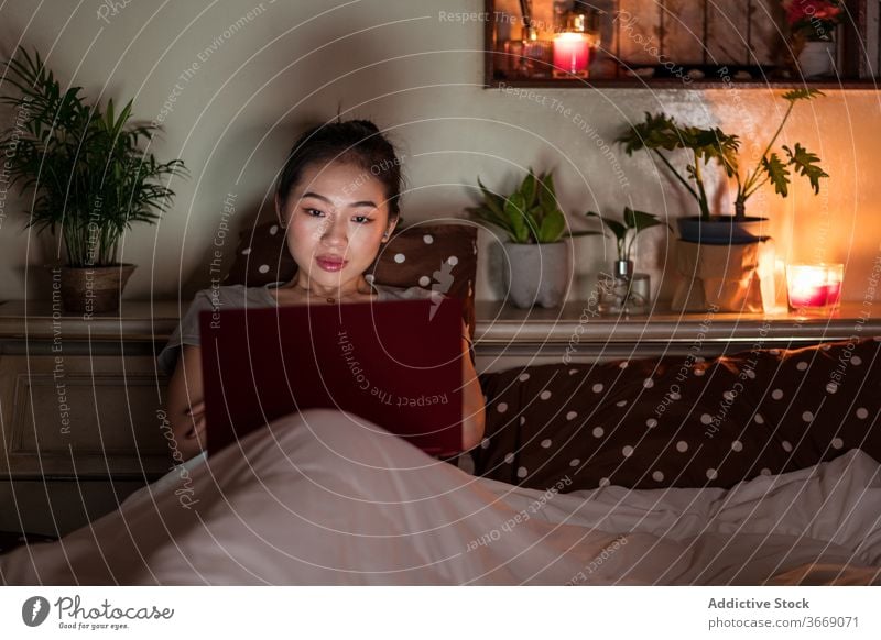 Asian woman sitting in bed with laptop at night relax internet comfort domestic using device gadget netbook enjoy charismatic screen browser positive happy