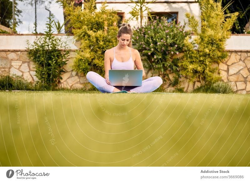 Tranquil woman using laptop on mat in courtyard online tutorial yoga choose pick tranquil sportswear female barefoot calm wellness healthy slim gadget device
