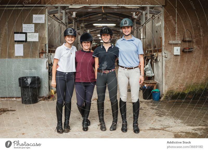 Company of jockeys in stable equestrian women together hug smile rider portrait friendly uniform barn equine young group unity company equipment friendship