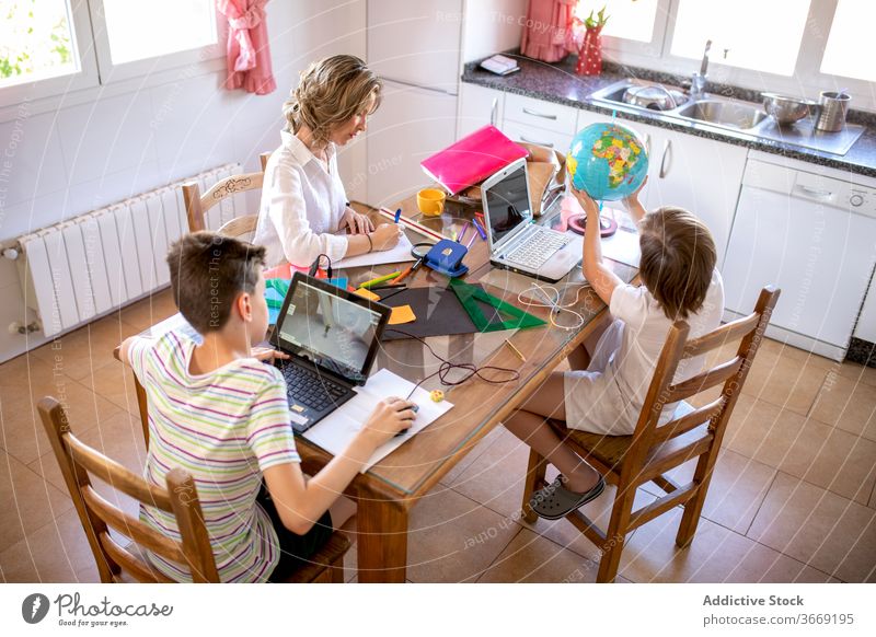 Serious businesswoman surfing internet on laptop with children at home mother typing homework education study lean on hand learn using gadget device netbook