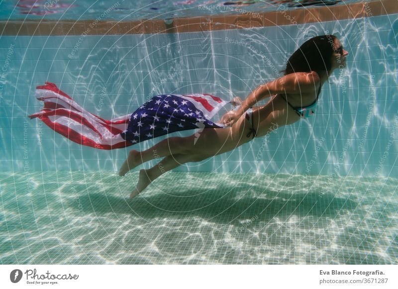 young woman in a pool holding american flag underwater. 4th july independence day concept. Summertime swimming pool summer sunglasses caucasian fun beautiful
