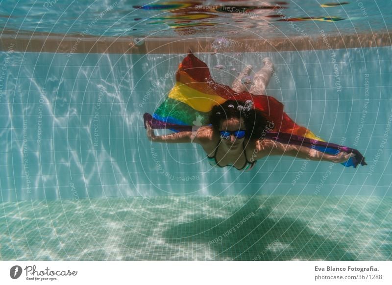 young woman in a pool holding rainbow gay flag underwater.LGBTQ concept. Summertime swimming pool love hugs lesbian homosexual equality attractive people female