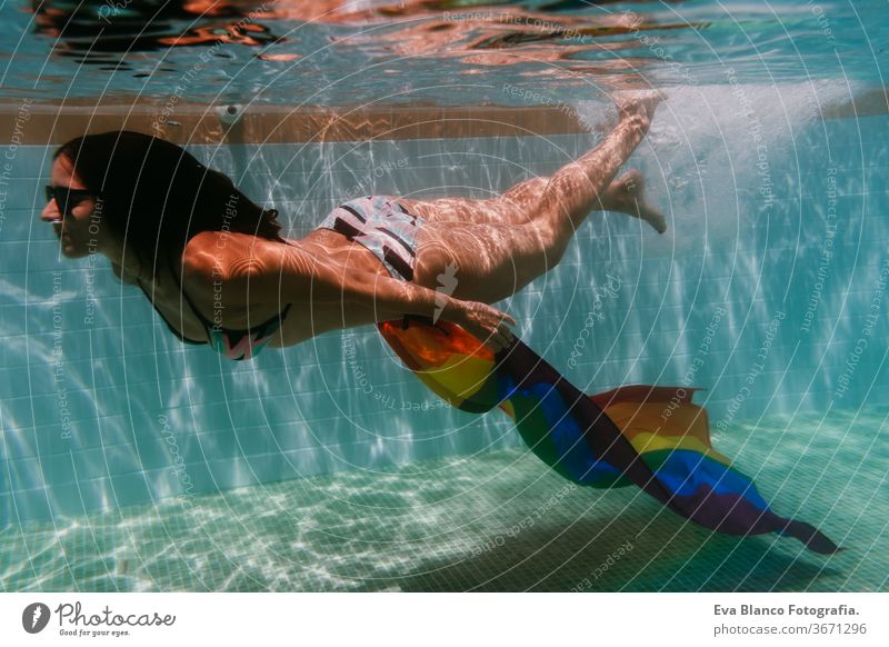 young woman in a pool holding rainbow gay flag underwater.LGBTQ concept. Summertime swimming pool love hugs lesbian homosexual equality attractive people female
