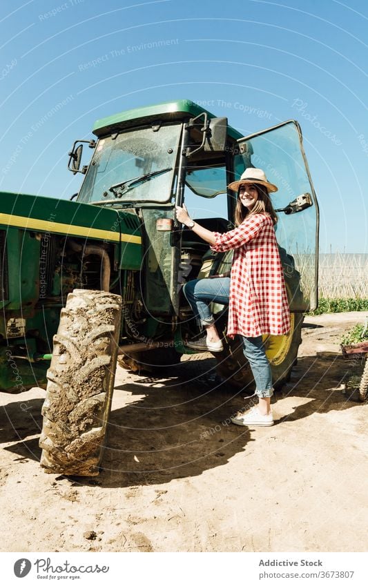 Glad woman getting on old tractor under blue sky get on positive sandy terrain summer countryside stand idyllic harmony weekend charming calm happy smile grass