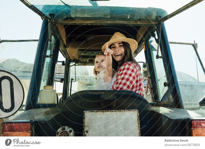 Happy woman embracing little child sitting in tractor in countryside mother embrace daughter childcare affection point finger bonding spend time motherhood