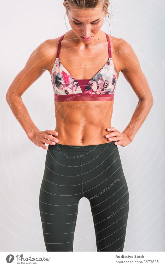Crop slim tired sportswoman in active wear having break indoors show abdomen six pack healthy wellbeing hand on waist slender sportswear belly stand fit