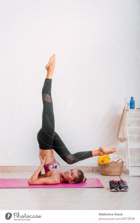Slim woman doing Salamba Sarvangasana pose on yoga mat practice supported shoulder stand pose balance vitality energy endurance barefoot wellness