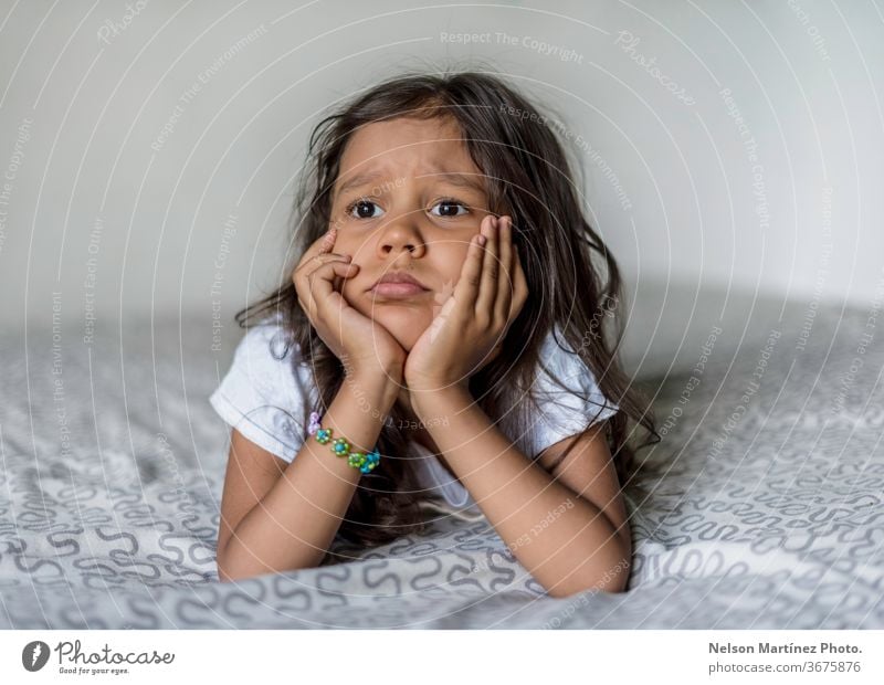 Portrait of a little hispanic girl. She is bored in her bed. She is looking to the window. summer young kids thinking boredom scholar coronavirus Boredom Child