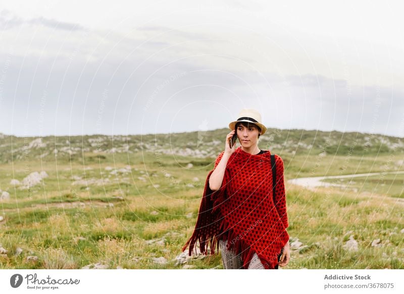 Stylish woman talking on smartphone in nature travel style call trendy mobile jesters of arenillas spain asturias llanes female poncho knitwear red lifestyle