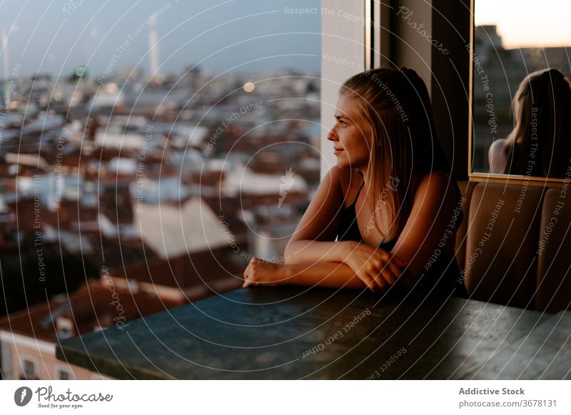 Young woman enjoying cityscape from cafe rooftop window evening madrid sunset cozy urban spain glass wall comfort relax restaurant reflection admire lounge