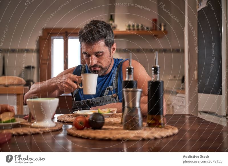 Mature man eating breakfast in kitchen delicious beverage enjoy mug drink cup calm hot tasty home food coffee relax healthy yummy mature morning fresh apartment