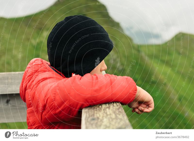 Little boy with red jacket and black cap leans over a balustrade and looks into the mountains Boy (child) Jacket Red Black green Hiking by hand Profile Looking