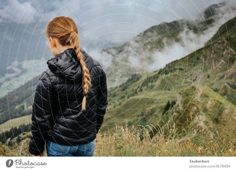 Girl with plait looks into a valley with clouds in the Alps in South Tyrol Child braid girl Blonde Observe Clouds Quilted jacket Small Black mountains green