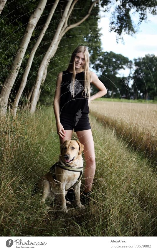 Portrait of a young woman in nature in front of a forest at the edge of a field with blond Labrador Purity luck Beautiful weather Trip Expectation Sunlight