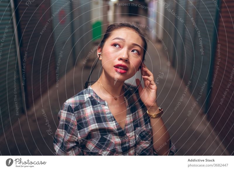 Woman with headset standing in underground corridor woman communicate talk casual urban asian ethnic millennial joy conversation lifestyle modern device gadget