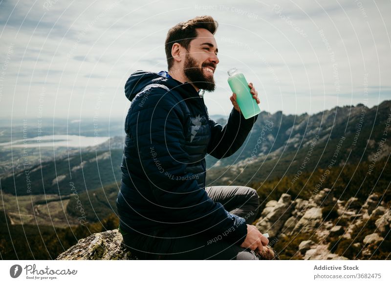 Happy male traveler drinking water in mountains man smile rest boulder puerto de la morcuera spain cheerful fresh bottle overcast sky vacation lifestyle sit