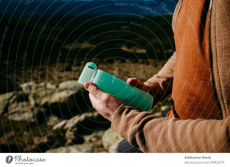 Anonymous male hiker with bottle of water in mountains man rest trip sky puerto de la morcuera thirst spain hydrate stone journey nature beverage stand rock