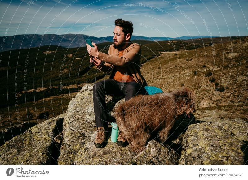 Bearded traveler with dog using smartphone in mountains man stone sit navigate puerto de la morcuera spain male connection rock browsing trip device gadget
