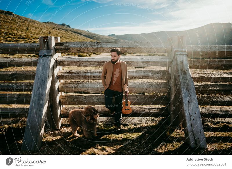 Male traveler with dog resting near fence man mountain lean sunny daytime puerto de la morcuera spain male countryside wooden owner ukulele barrier relax nature