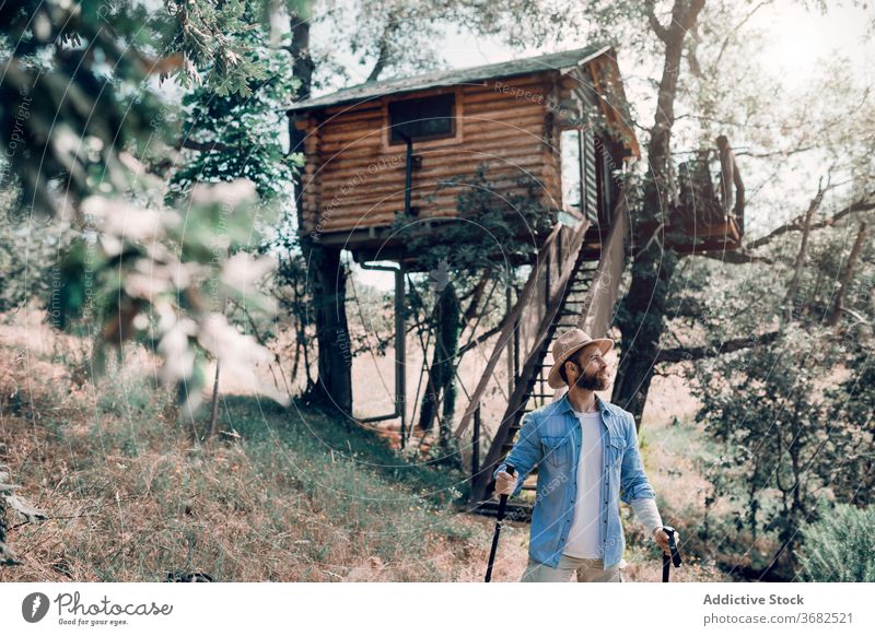 Traveling man with trekking poles in forest traveler hike tourist nature vacation summer male tree woods green hut carefree tourism journey house trip