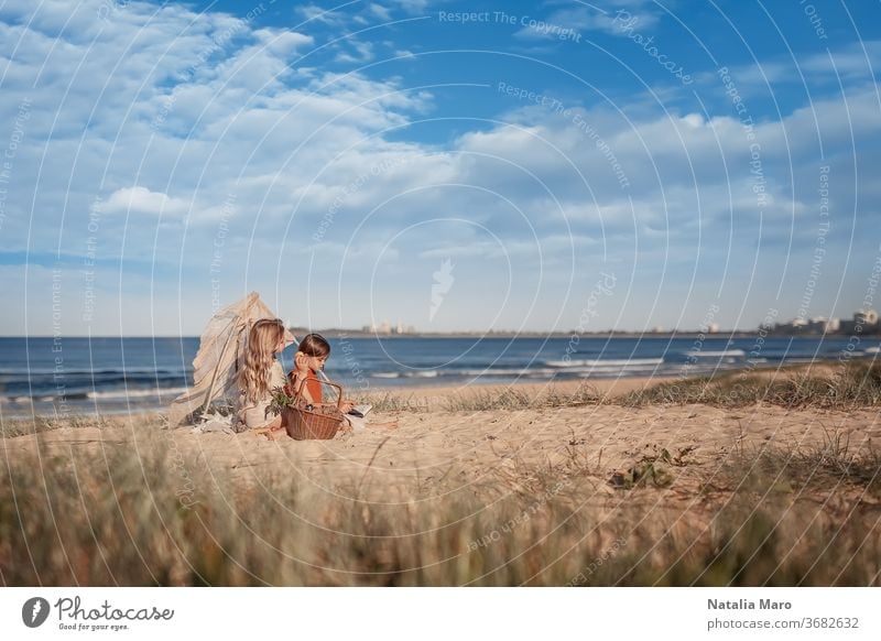 Two little girls having picnic, sitting in a small wigwam or hut of branches on the sandy Australian ocean beach kid happy nature summer teepee water white