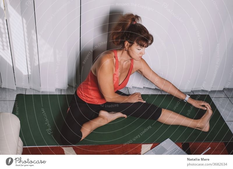 Attractive middle-aged woman doing yoga at home, having lesson online. Stay healthy during the quarantine lockdown women middle aged exercising stretch