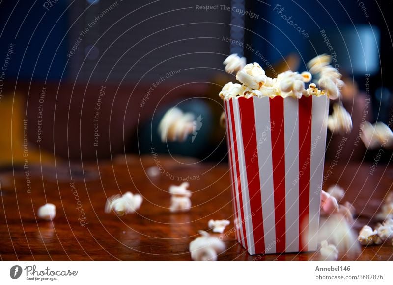 Popcorn flying out of cardboard box. red and white striped popcorn bucket with flying popcorn in the living room, movie or cinema concept snack falling