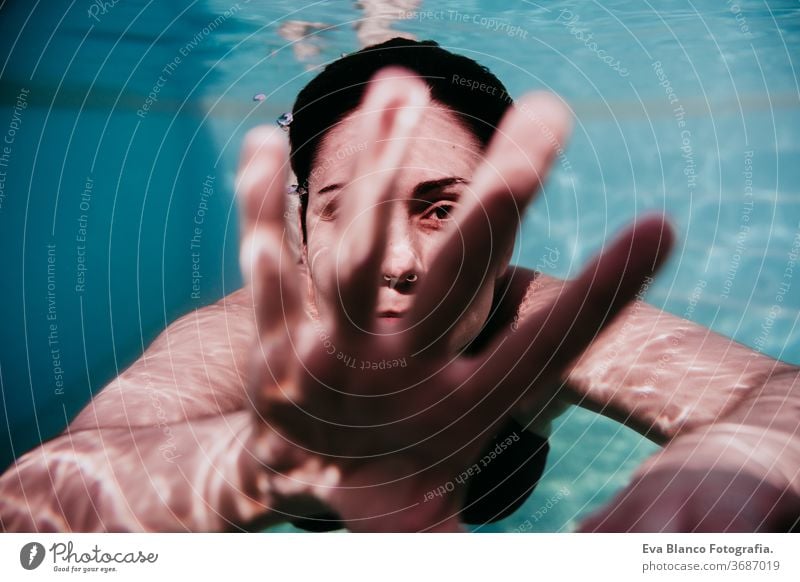 portrait of young woman diving underwater in a pool. summer and fun lifestyle touching hand swimming bubbles caucasian dive clear health light action wet