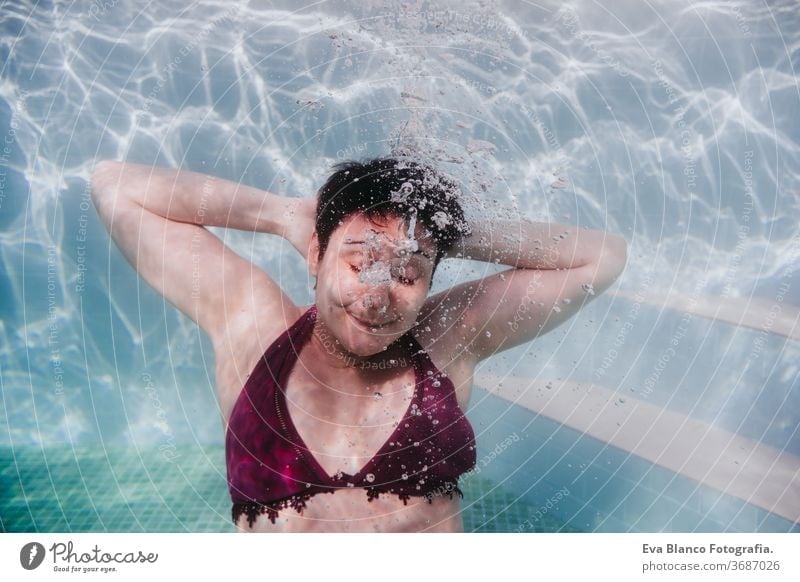 young woman diving underwater in a pool. arms resting behind the head. summer and fun lifestyle portrait close up swimming bubbles caucasian dive clear health
