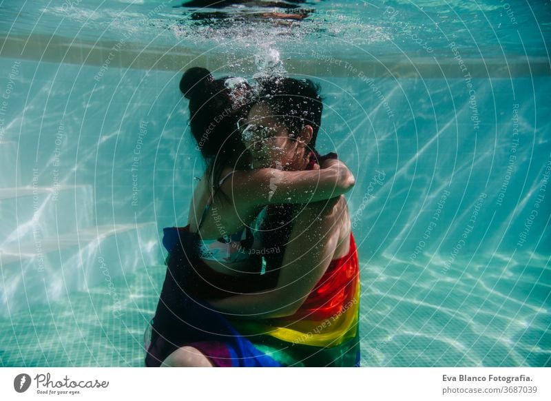 two women at the pool together wrapped with rainbow gay flag. LGBT concept love lesbian underwater swimming pool floating summer lgbt dating romantic bisexual