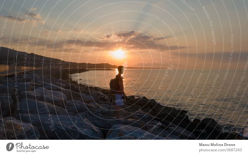 Young boy next to a jetty by the sea at sunrise young person human beach coast water dawn sky yellow orange blue early day mediterranean tranquility thought
