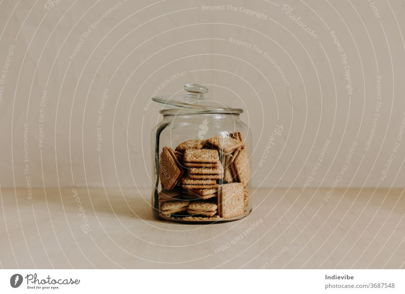 A glass jar of biscuit on wooden table with beige background cookie sweet snack healthy unhealthy dessert tasty processed sugar treat baked cake brown diet