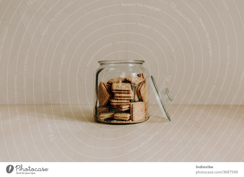 A glass jar of biscuit on wooden table with beige background cookie sweet snack healthy unhealthy dessert tasty processed sugar treat baked cake brown diet