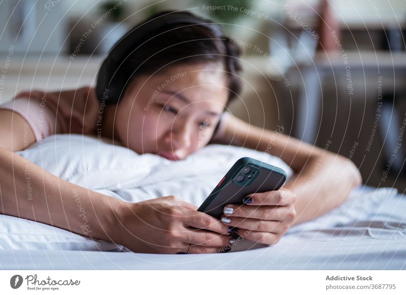 Sad Asian female browsing smartphone on bed woman using sad social media cozy lying read bedroom home unhappy ethnic comfort mobile device gadget internet