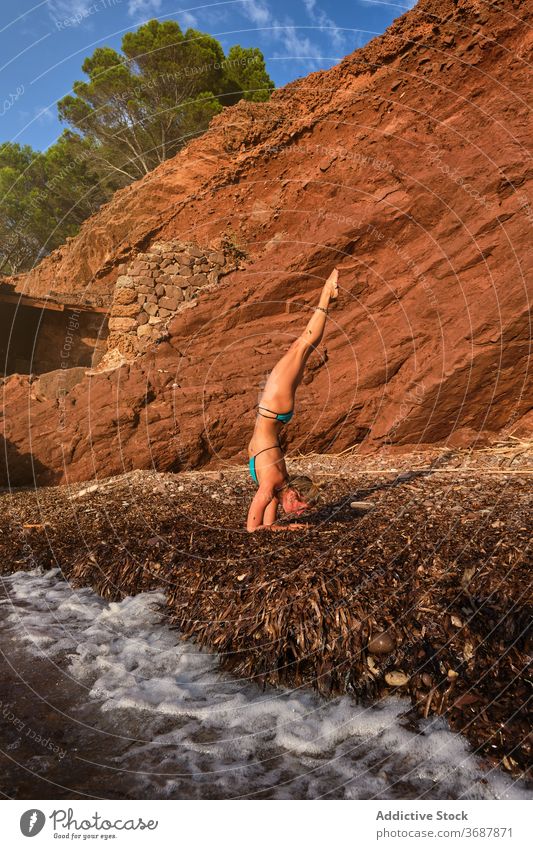 Woman doing a variation of the Handstands yoga pose on a beach vertical wave sea motion natural forest inverse handstand fitness sport strength health woman