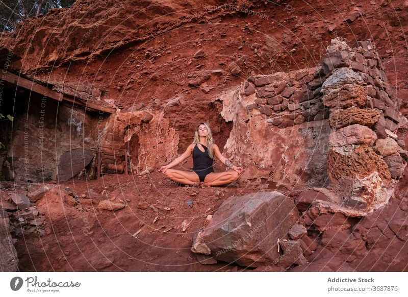 Woman in a swimsuit sitting in meditation in the ruins of a house in an arid terrain ancient remain surface isolated abandoned yoga nature fitness meditating