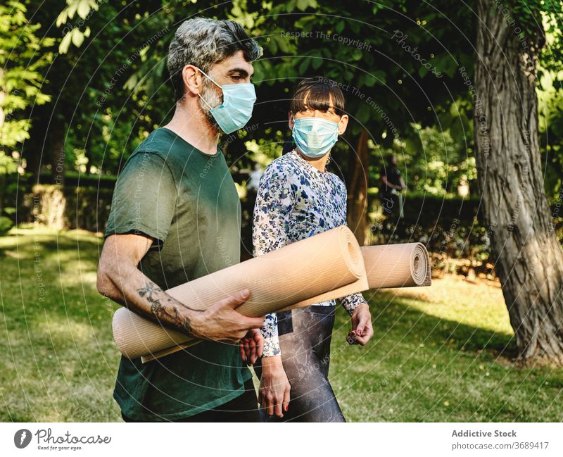 Cheerful couple with medical masks and yoga mats walking in park cheerful together coronavirus covid pandemic covid19 new normal infection positive talk happy