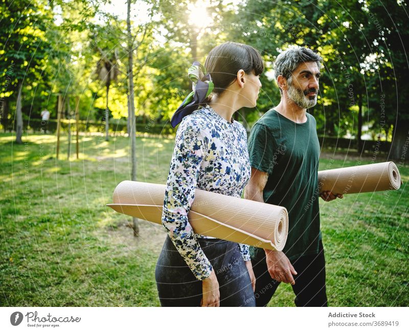 Cheerful couple with yoga mats walking in park cheerful together positive talk happy communicate conversation practice wellness activity nature content enjoy