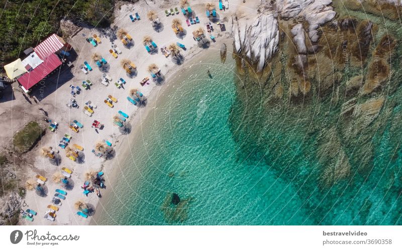 Mediterranean Greek landscape drone shot at Kavourotripes beach with bathers. Sithonia Chalkidiki peninsula aerial top view with rocky coastal, crystal clear waters & sea beds with umbrellas.