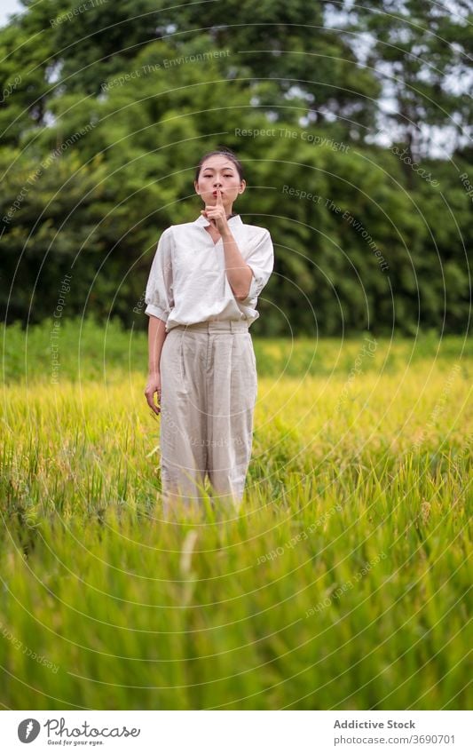 Ethnic woman showing silence gesture in field silent hush lip rice nature sign calm female asian ethnic secret shh charming stand peace tranquil finger on lips