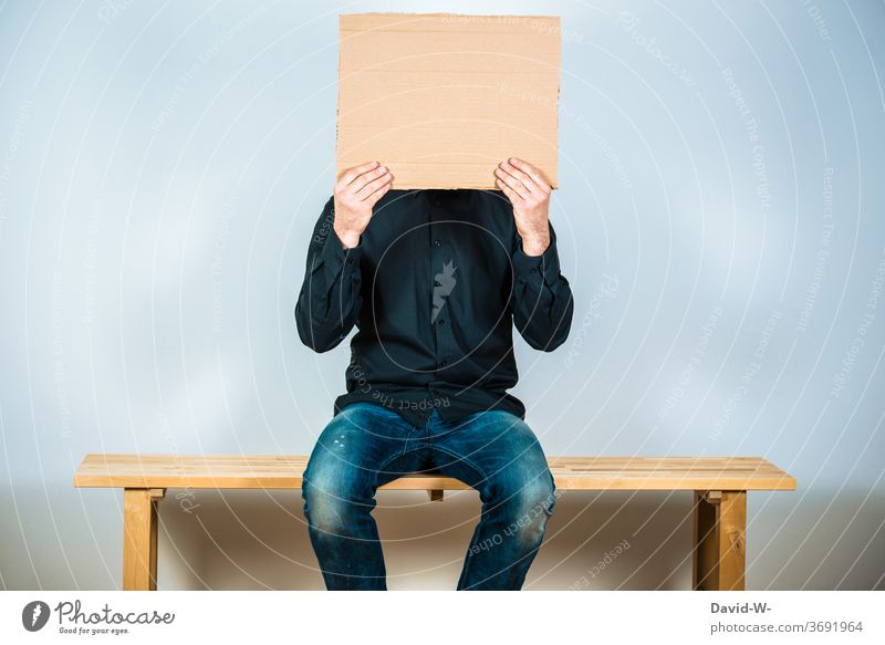 Man holds a sign up to his face sedentary Sit waitWaiting room cardboard box Placeholder Copy Space Neutral Anonymous Manly Human being Life Colour photo