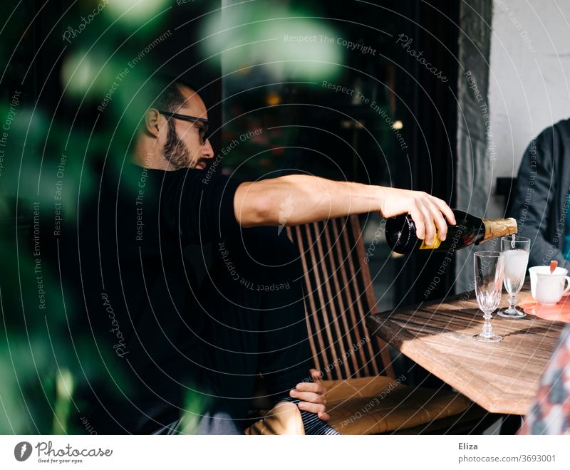 A man sits at a table in the garden and pours prosecco into glasses Prosecco Garden bottle Sparkling wine Champagne bottle celebration Day Drinking Pour Table