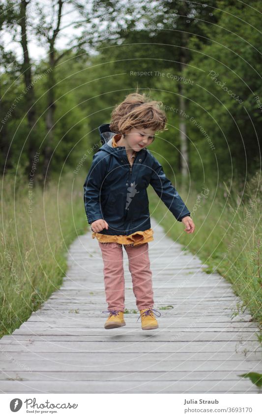 Infant flying in the air in a raincoat on a wooden plank Toddler girl Flying Free Joy hair Wild Departure Funny Grinning Romp Playing Lanes & trails off