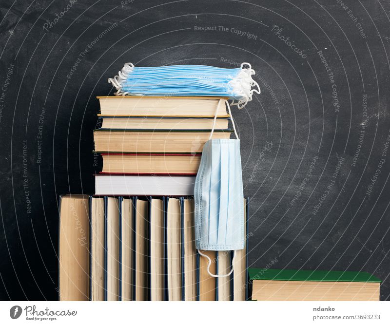 stack of various books and disposable medical masks on the background of an empty black chalk board white wooden virus school nobody education study home